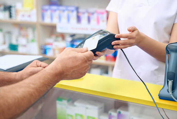 Closeup of a Pharmacist holding terminal while a man pays with a credit card.